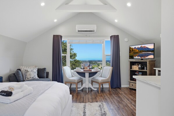 Ein Schlafzimmer mit Bett, Esstisch mit Stühlen, Fernseher und Blick ins Freie.