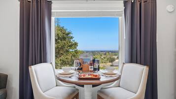 Un comedor con una mesa, dos sillas, una ventana con cortinas y vistas al campo.