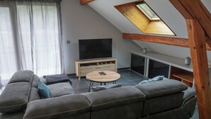 A modern living room with a large gray sofa, a small round coffee table, a TV on a wooden stand, and a skylight above.