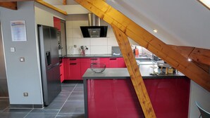 A modern kitchen with red cabinets, stainless steel appliances, and a wooden ceiling beam.