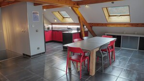A modern kitchen with red cabinets, a dining area with a wooden table and red chairs, and skylights.