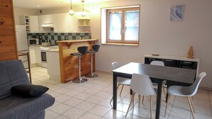 Un espacio habitable compacto con kitchenette, una zona de comedor con mesa y sillas, y un sofá con cojín.