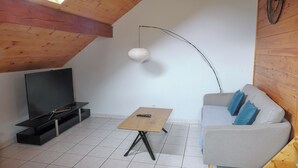 A cozy living room with a TV, a wooden coffee table, a sofa with cushions, and a unique curved ceiling light.