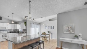 A modern kitchen with a central island, bar stools, and a dining area with a table and chairs.