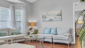 A modern living room with a sofa, a round glass coffee table, and a ceiling fan.