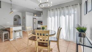 A modern kitchen with white cabinets, a dining area with a round table and chairs, and a living space with a large window and curtains.