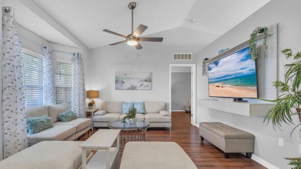 A modern living room with a ceiling fan, a flat-screen TV, a sofa, a coffee table, and a bench.