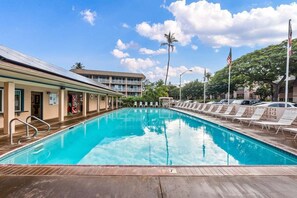 Une piscine avec des chaises longues et, au fond, un bâtiment doté d’un balcon.