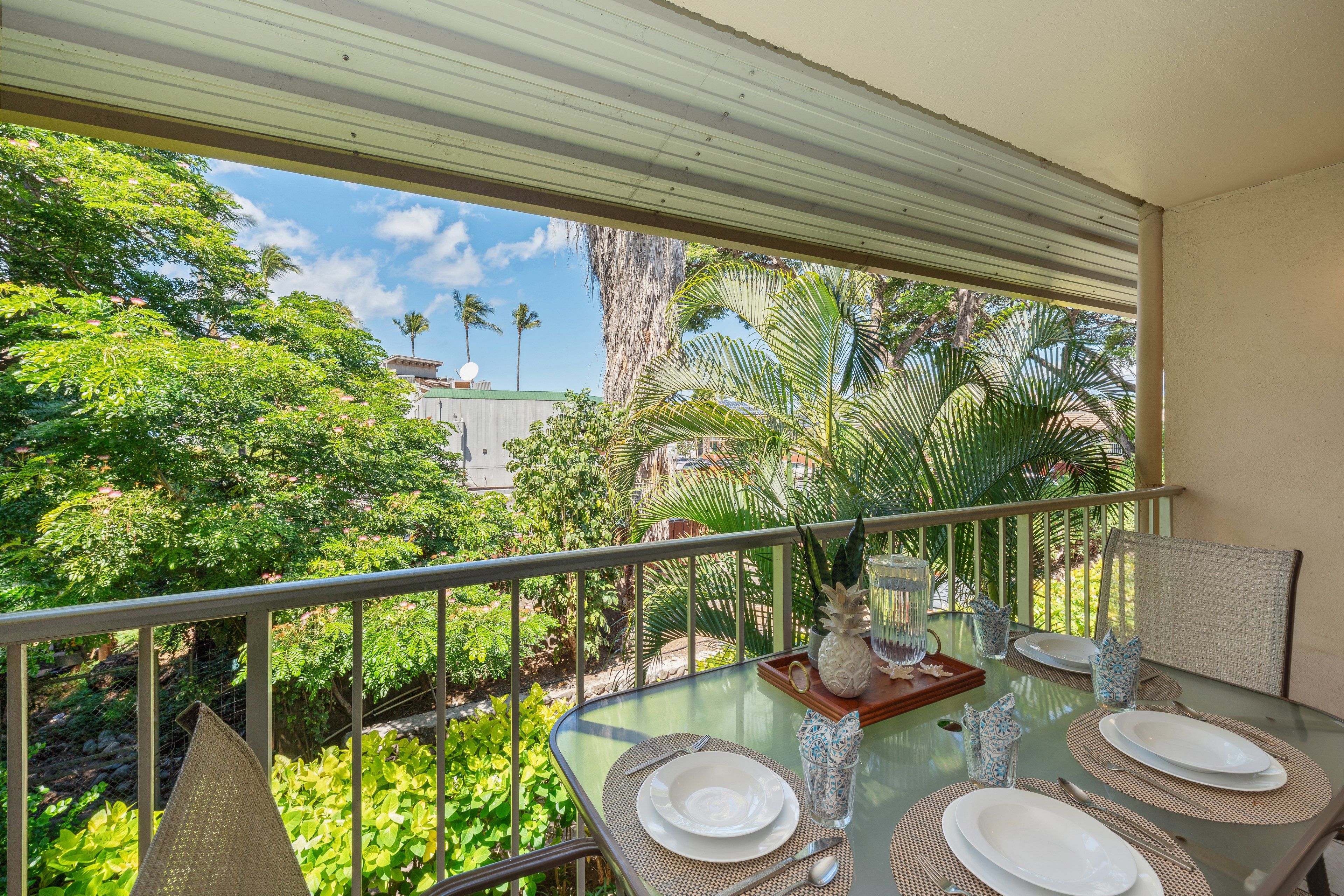A glass table set for dining with a view of tropical vegetation and a building in the background.