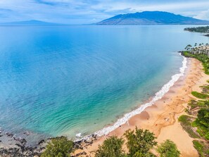 Una playa costera con aguas transparentes, una orilla arenosa y montañas al fondo.