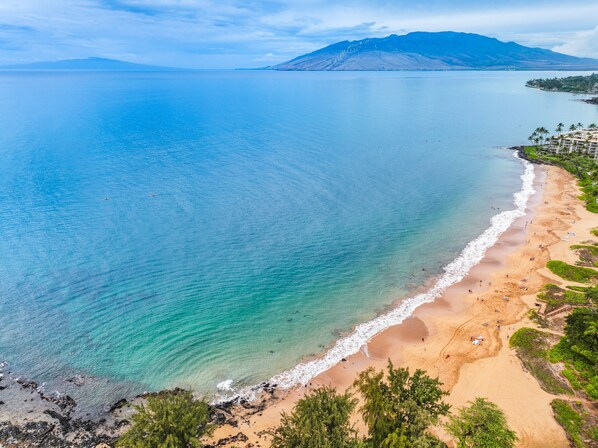 A coastal beach with clear waters, a sandy shore, and a mountainous backdrop.