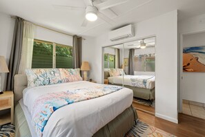 A bedroom with a large bed, a ceiling fan, a window with curtains, and a mirror reflecting the room.
