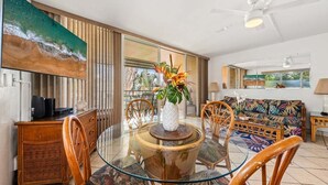Un comedor con mesa de vidrio, sillas de mimbre y sofá con motivos tropicales.