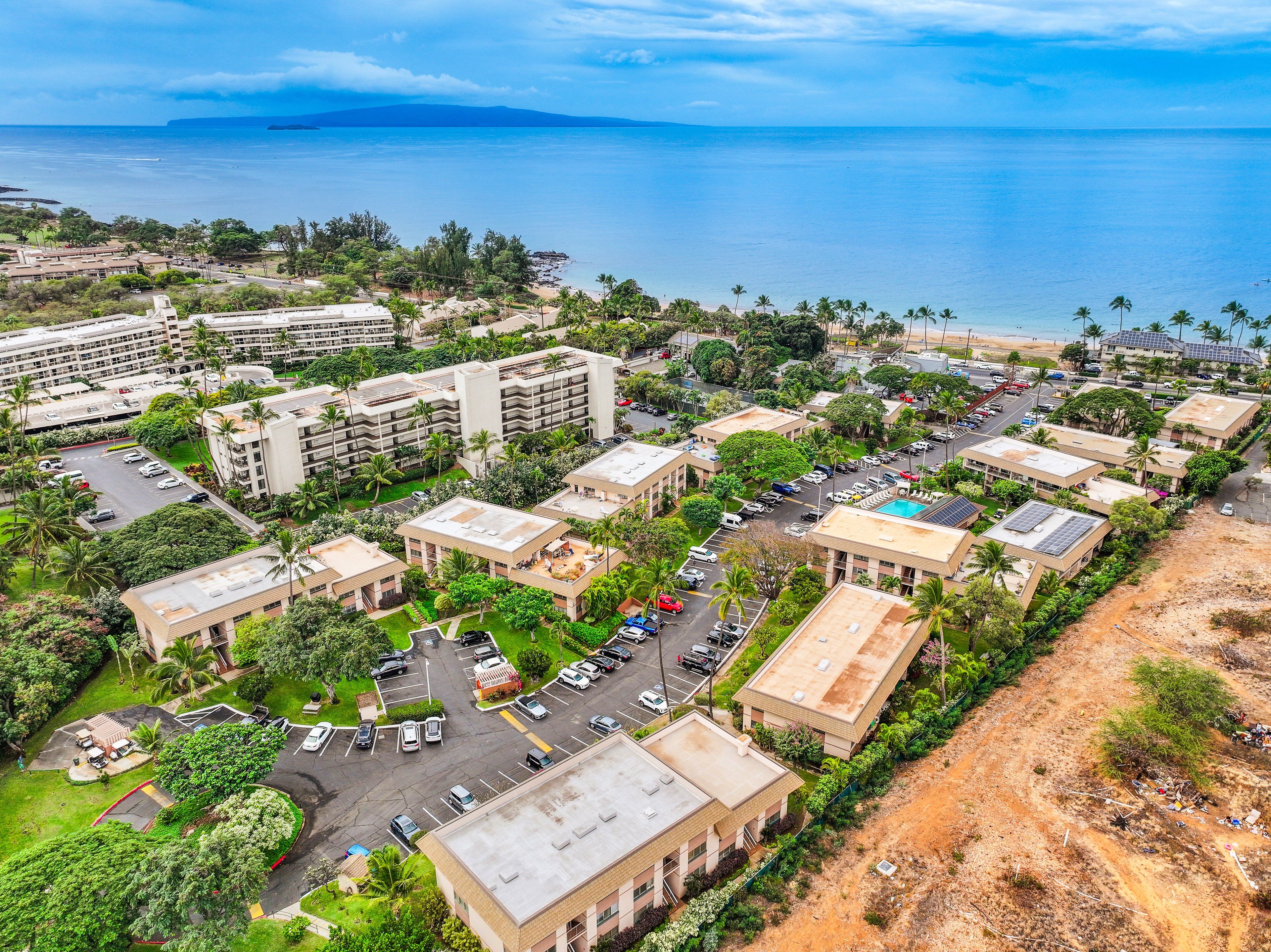 Vista aérea de un complejo turístico frente al mar, con varios edificios, zonas de estacionamiento y una playa.