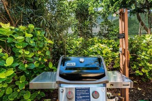 Ein Weber Spirit II Grill mit einer Metall-Tischplatte, umgeben von üppigem Grün.
