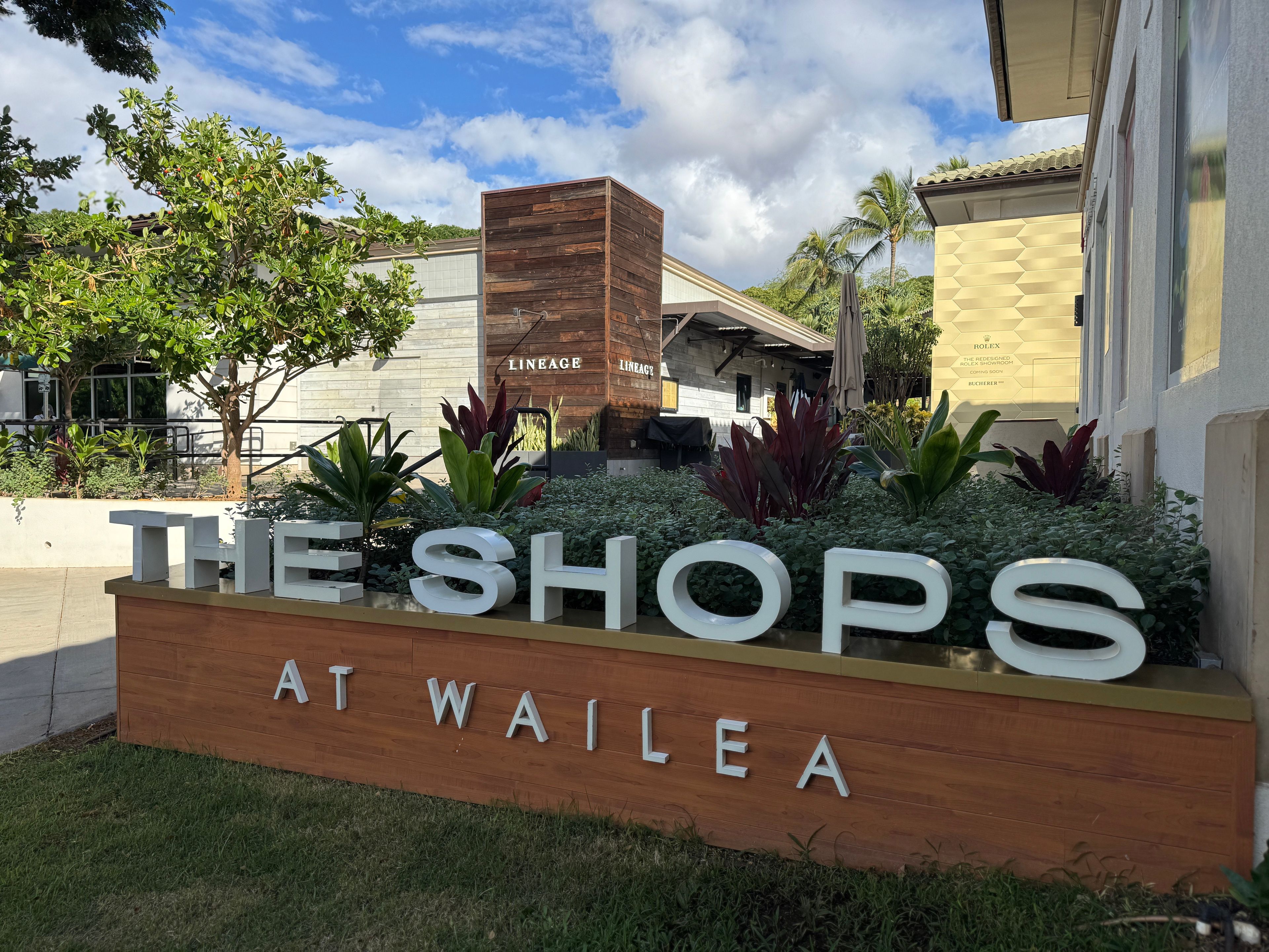 Schild für 'The Shops at Wailea' mit Holzkonstruktion und Grünpflanzen.