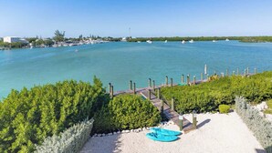 A coastal view with a wooden pier leading to a sandy beach, surrounded by greenery and calm waters. - Luxury Marathon Waterfront Home | Pool & Dock (Marathon)