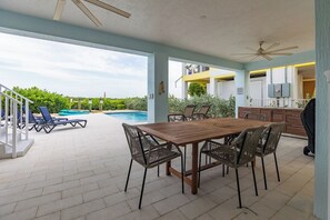 An outdoor patio with a pool, a dining table with chairs, and a ceiling fan. - Luxury Marathon Waterfront Home | Pool & Dock (Marathon)