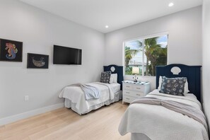A bedroom with two beds, a TV, artwork, and a window with a view.