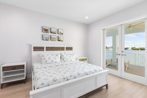 A bedroom with a bed, a nightstand, a dresser, and a view of a balcony with a railing.