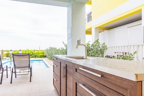 An outdoor kitchen area with a built-in sink, adjacent to a poolside seating area. - Luxury Marathon Waterfront Home | Pool & Dock (Marathon)