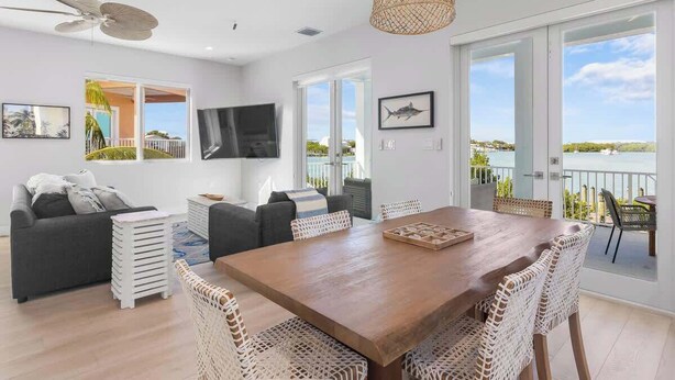 A spacious living area with a wooden dining table, wicker chairs, a grey sofa, and a TV. - Luxury Marathon Waterfront Home | Pool & Dock (Marathon)