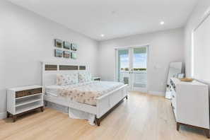 Ein Schlafzimmer mit Bett, Nachttisch, Kommode und Balkontür.