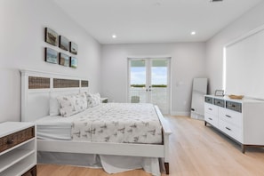 Ein Schlafzimmer mit Bett, Kommode, Spiegel und Balkontür.