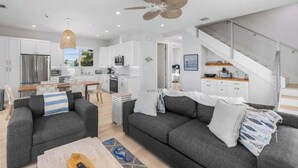 A modern kitchen with white cabinets, a dining area with a table and chairs, a living room with a sofa and a coffee table, and a staircase leading to an upper level. - Luxury Marathon Waterfront Home | Pool & Dock (Marathon)