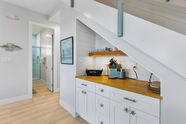 A modern kitchen with white cabinetry, a wooden countertop, and a built-in coffee station.