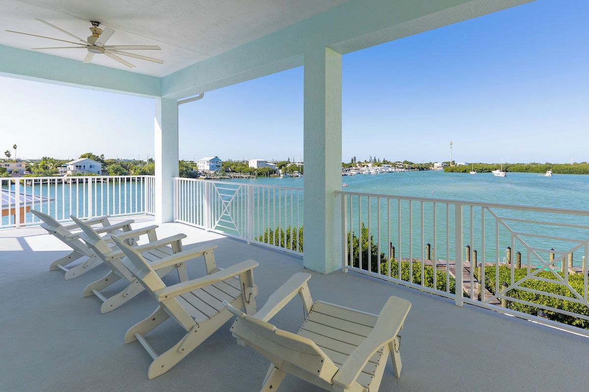 A covered balcony with white railings and a view of the sea.