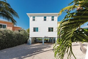 A two-story building with a flat roof, a gravel driveway, and a palm tree in the foreground.
