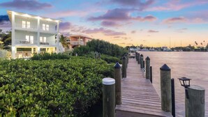 A wooden pier leading to a multi-story building with balconies, surrounded by lush greenery and a calm waterfront. - Luxury Marathon Waterfront Home | Pool & Dock (Marathon)