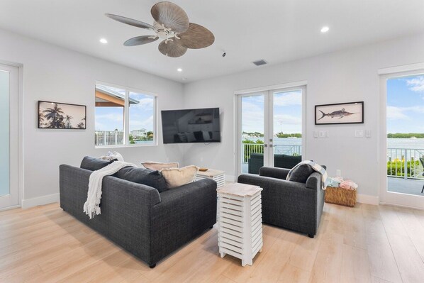A modern living room with a grey sofa set, a flat-screen TV, and a ceiling fan. - Luxury Marathon Waterfront Home | Pool & Dock (Marathon)