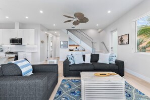 A modern living space with a kitchen, a grey sofa, a coffee table, and a staircase leading to an upper level.