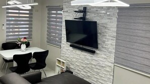 A modern living room with a sectional sofa, a flat-screen TV mounted on a textured wall, and pendant lighting. - American Standard/2Bedroom House (Cagayan de Oro)