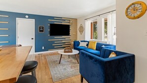 Una sala de estar moderna con un sofá azul, una mesa de comedor de madera y un televisor de pantalla plana montado en la pared.