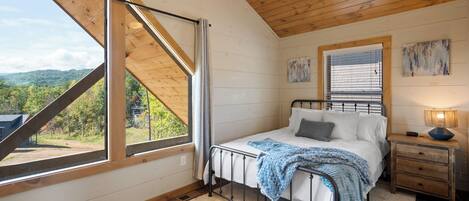 A bedroom with a bed, a nightstand, a window with a view of the outdoors, and a ceiling fan.