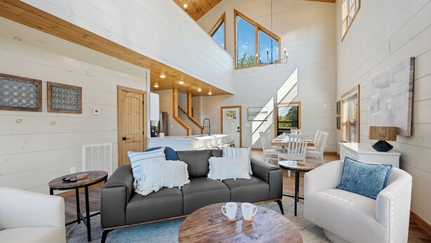 A spacious living area with a high ceiling, wooden beams, a gray sofa, a white armchair, and a round coffee table. - New cabin! Great Location! 5 Min to Parkway! Private pool, hot tub, & game room! (Pigeon Forge)
