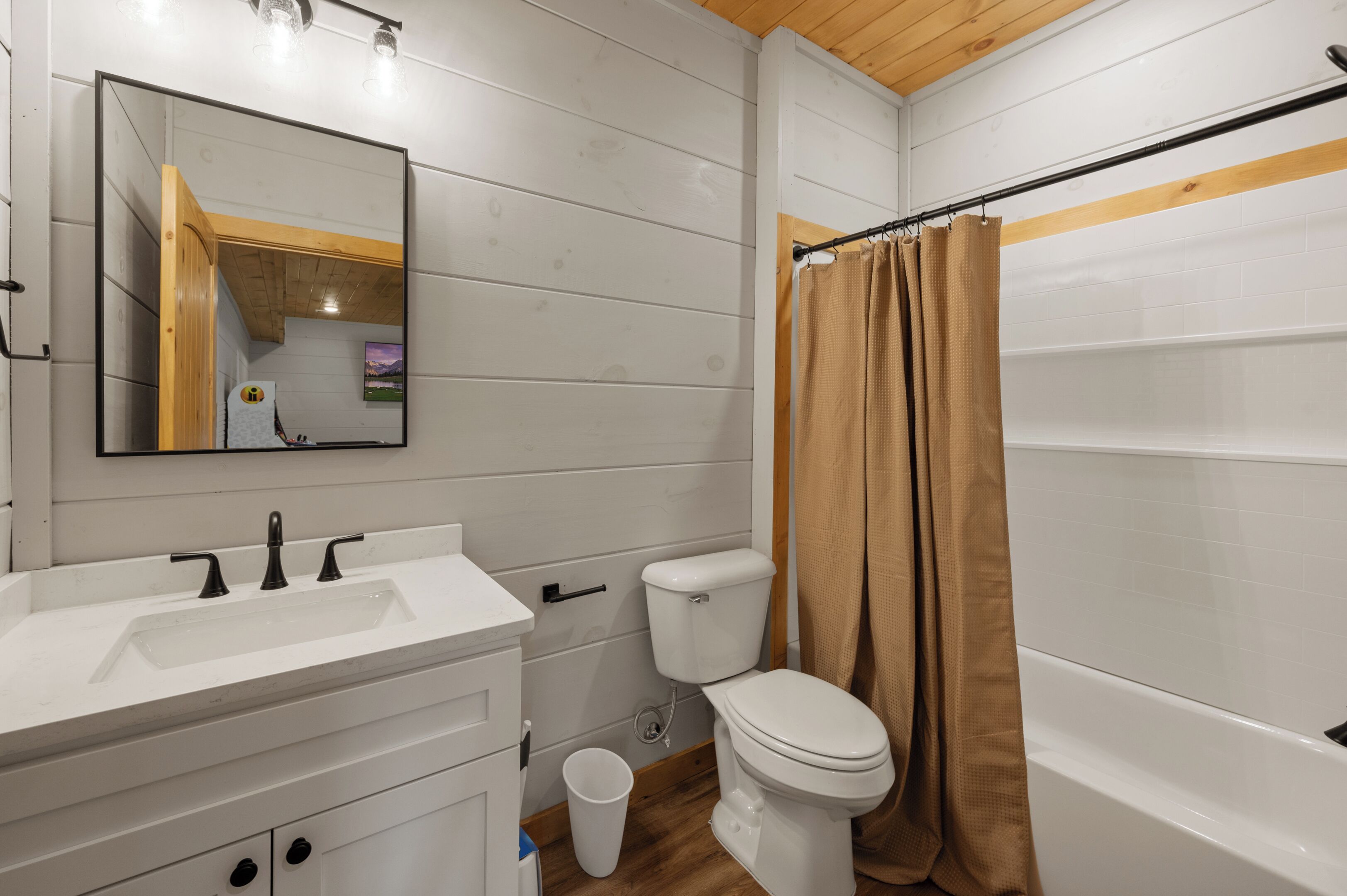 Baño con lavamanos blanco, espejo, inodoro y cortina de ducha.