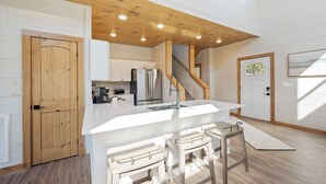 A modern kitchen with white cabinetry, stainless steel appliances, and a wooden ceiling. - New cabin! Great Location! 5 Min to Parkway! Private pool, hot tub, & game room! (Pigeon Forge)