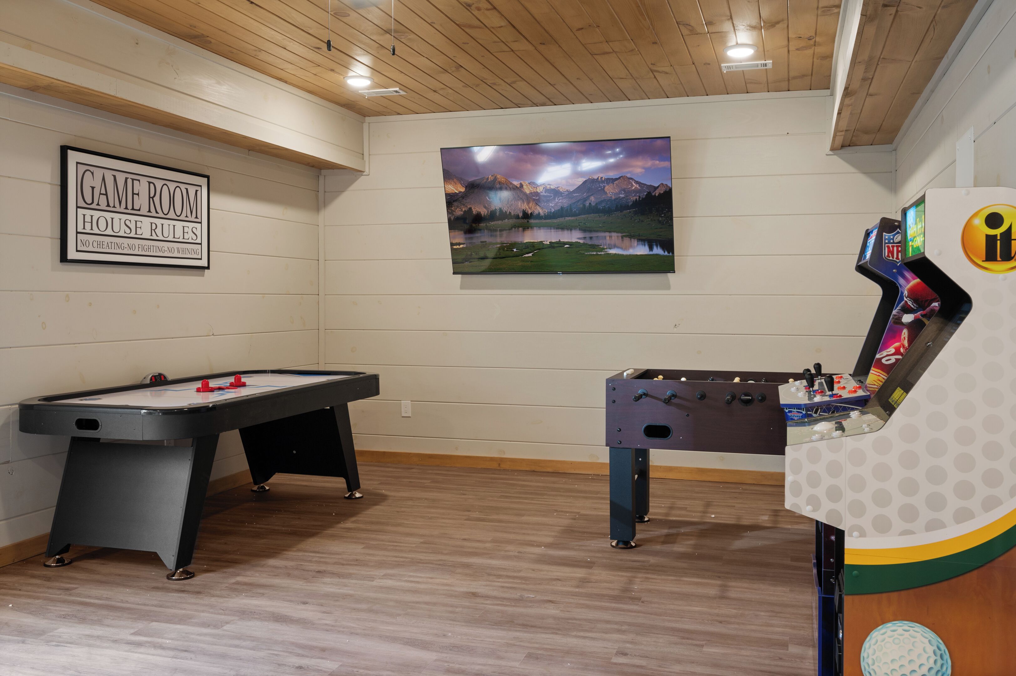 A game room with a pool table, foosball table, and a large TV displaying a scenic landscape.