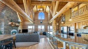 Ein großzügiges Holzblockhaus-Interieur mit Kamin aus Naturstein, ein geräumiger Wohnbereich mit einer Couch, eine Küche mit modernen Geräten und ein Balkon mit Aussicht.