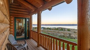 Eine Holzhütte mit Veranda, zwei Adirondack-Stühlen und Blick auf einen See und Berge.