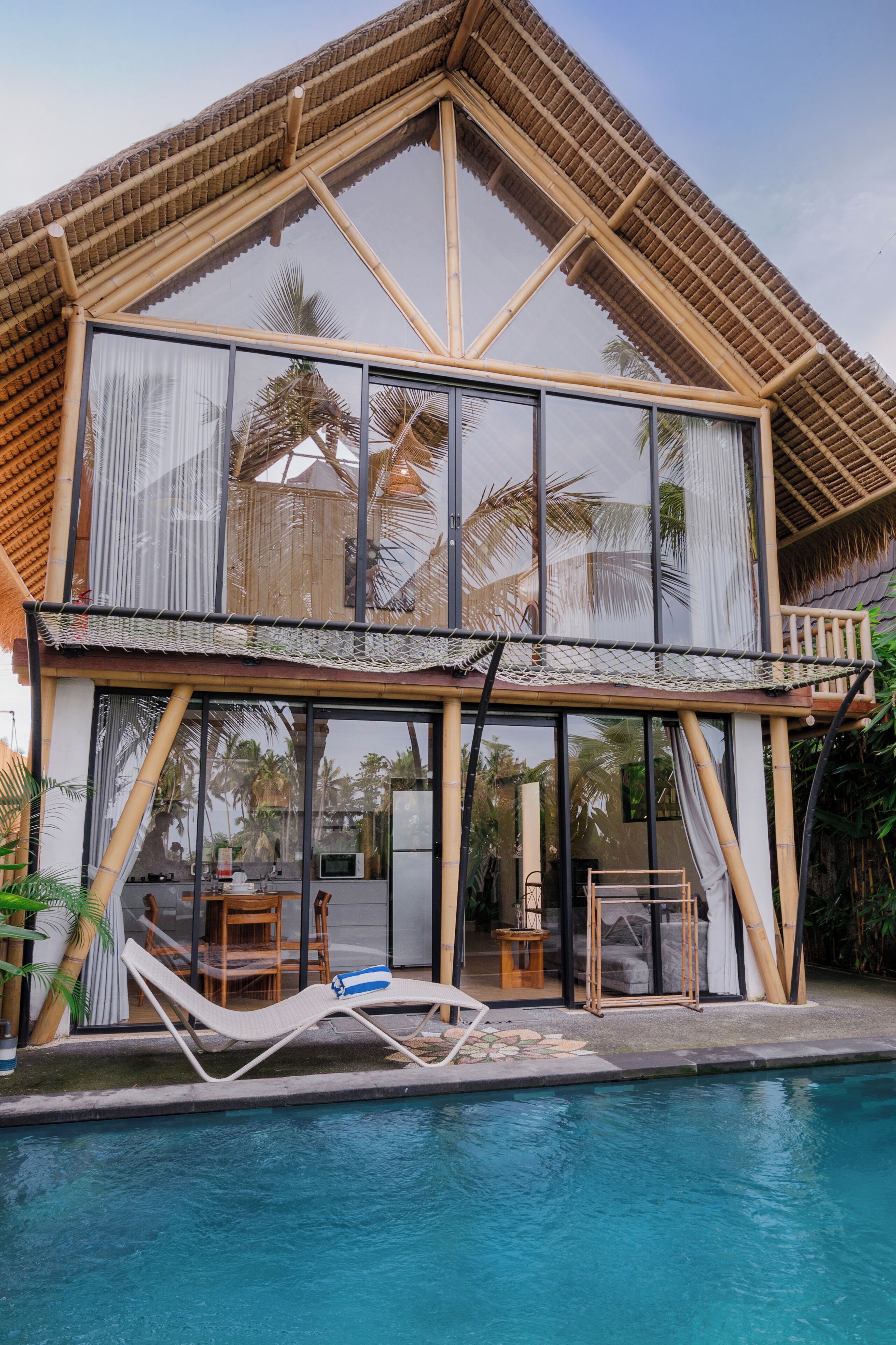 A modern house with a large glass window, a pool, and a dining area.