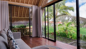 Amplia habitación con un gran ventanal corredero que da a un jardín exuberante, un sofá cómodo con cojines estampados y un techo de madera.