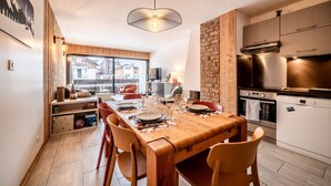 Uma cozinha moderna com eletrodomésticos de aço inoxidável, uma mesa de jantar de madeira posta para quatro pessoas e vista para o exterior através de grandes janelas.