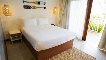 A bedroom with a wooden bed, white bedding, a nightstand, a woven rug, and a view of the outdoors through a sliding door.