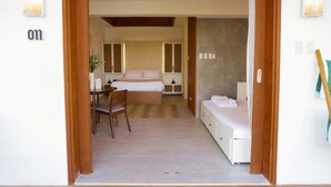A hotel room with a bed, a desk with a chair, a small table with a vase, and a bathroom with a shower curtain. - Caza Guesthouse Iyang (Concepcion)