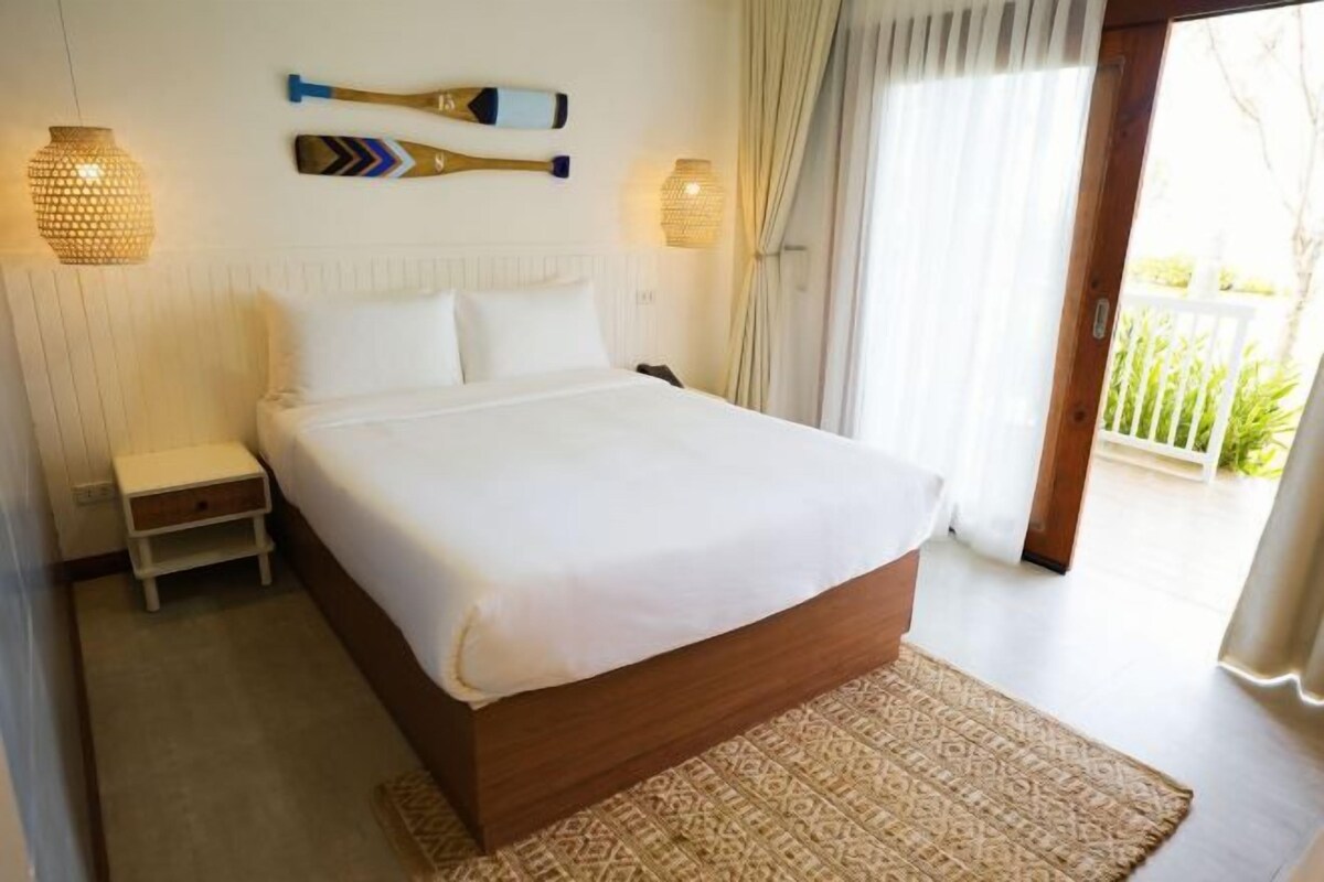 A bedroom with a large bed, a bedside table, a patterned rug, and a view of the outdoors.